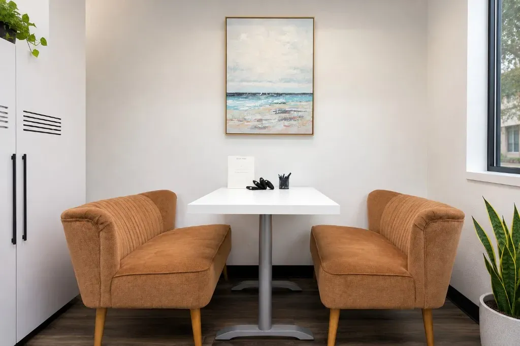 Shared breakout space with facing loveseats, pedestal table, and coastal wall art