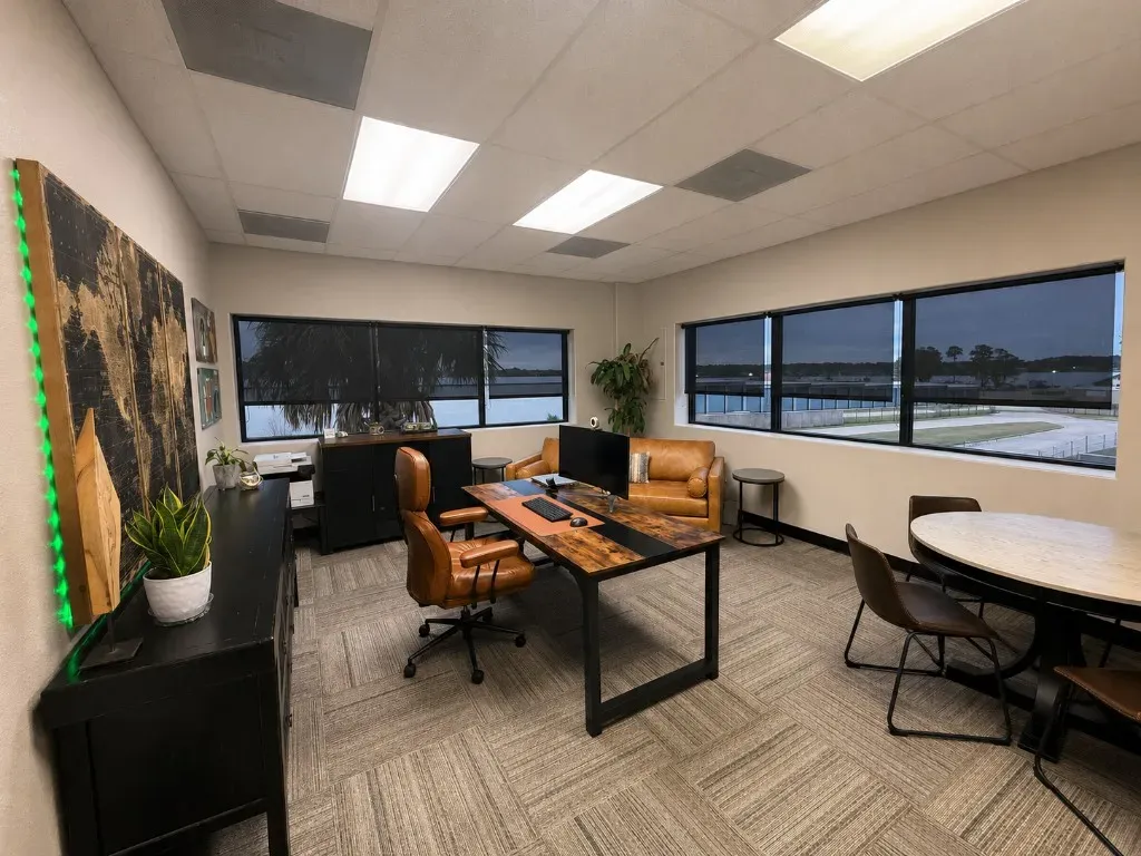 Corner private office with lake view windows, desk, seating area, and round meeting table