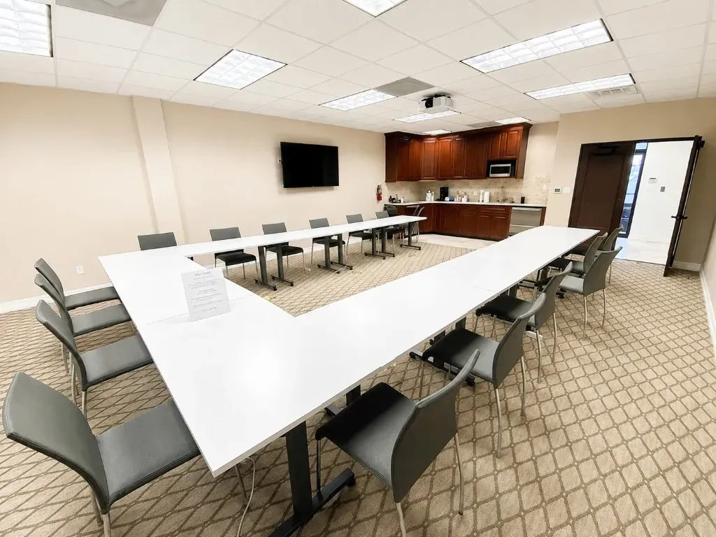 Conference meeting room with U-shaped tables, seating, and presentation screen