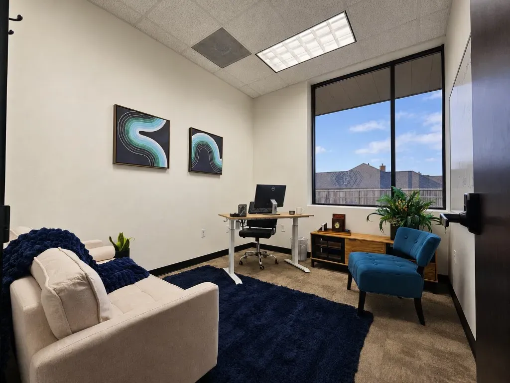 Bright private window office with standing desk, sofa, and guest seating